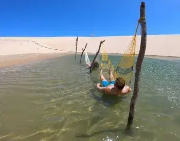 Duas pessoas relaxando em duas redes em uma lagoa entre as dunas